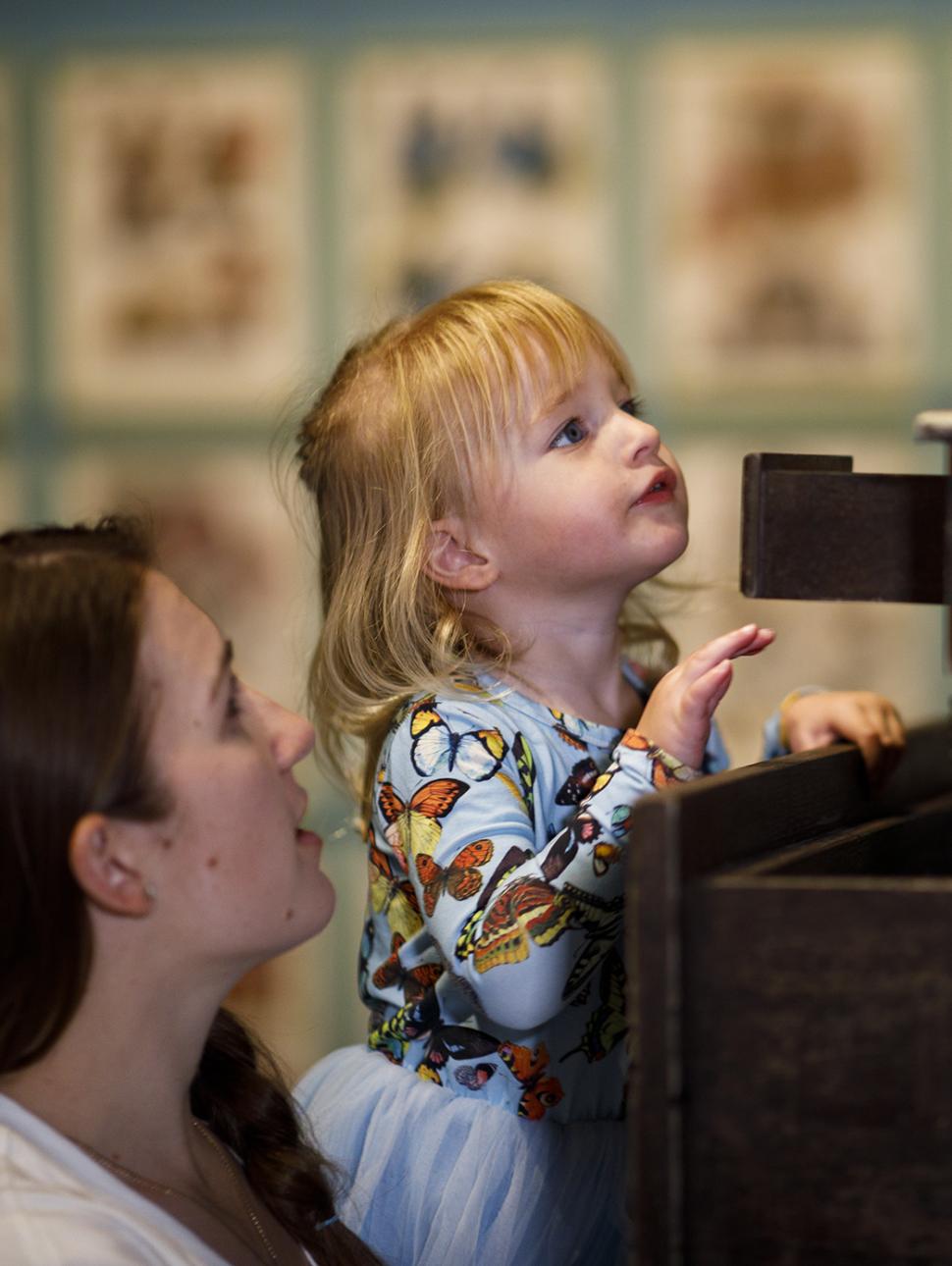 Small child is looking up over their hands at a prop with a parent nearby