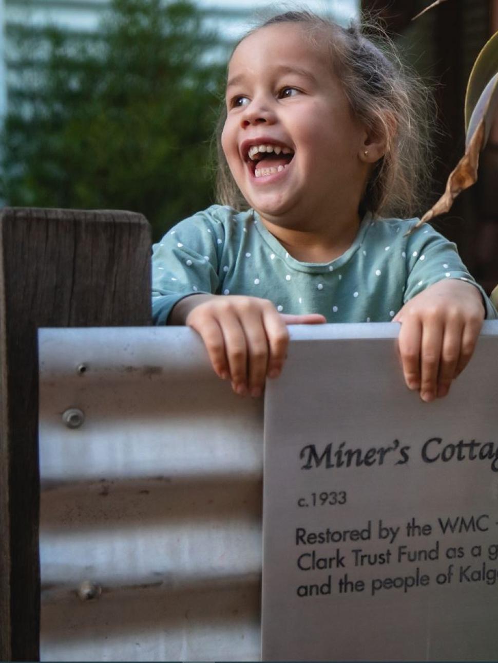 Child holding onto a metal dence laughing with a garden behind her