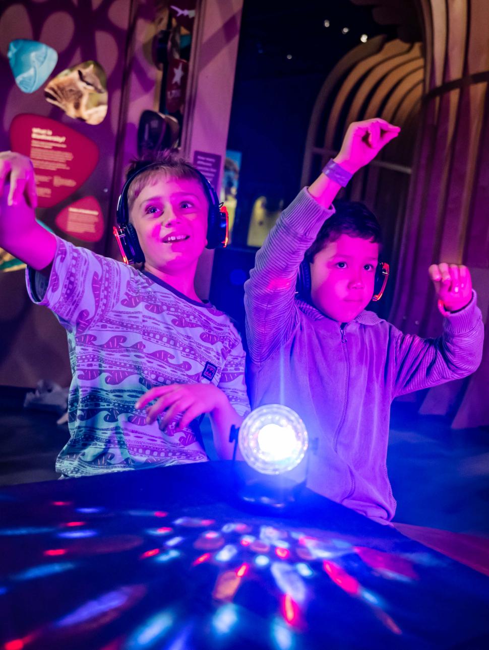 Two kids dancing in pink light with headphones on