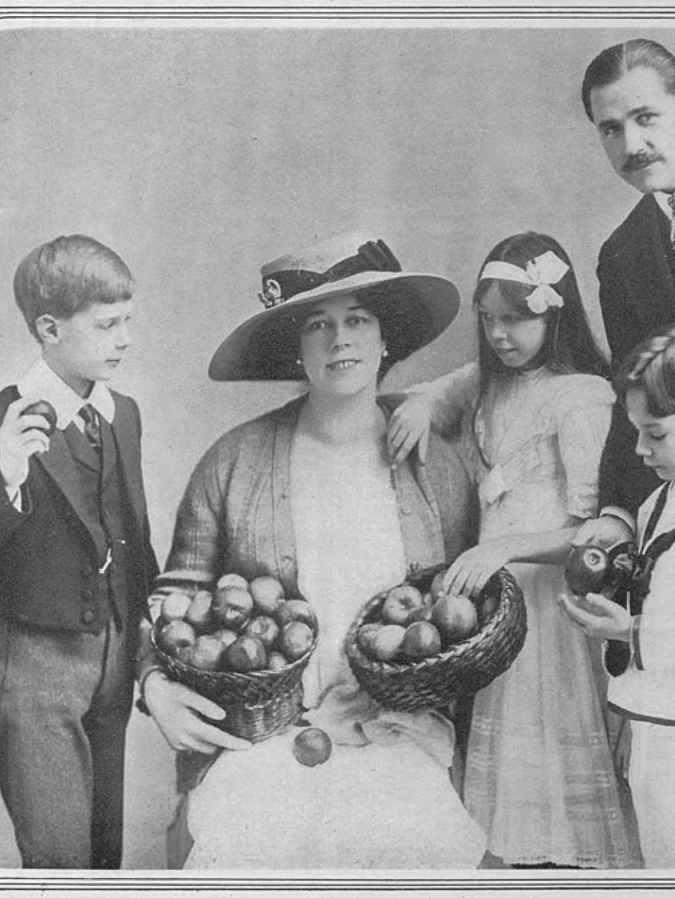 A black and white image of Clare Butt wearing a white vintage dress and hat posing with her family