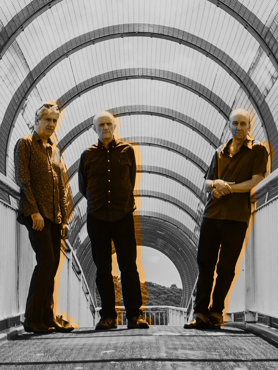 Three men standing on a bridge with round mental structures behind 