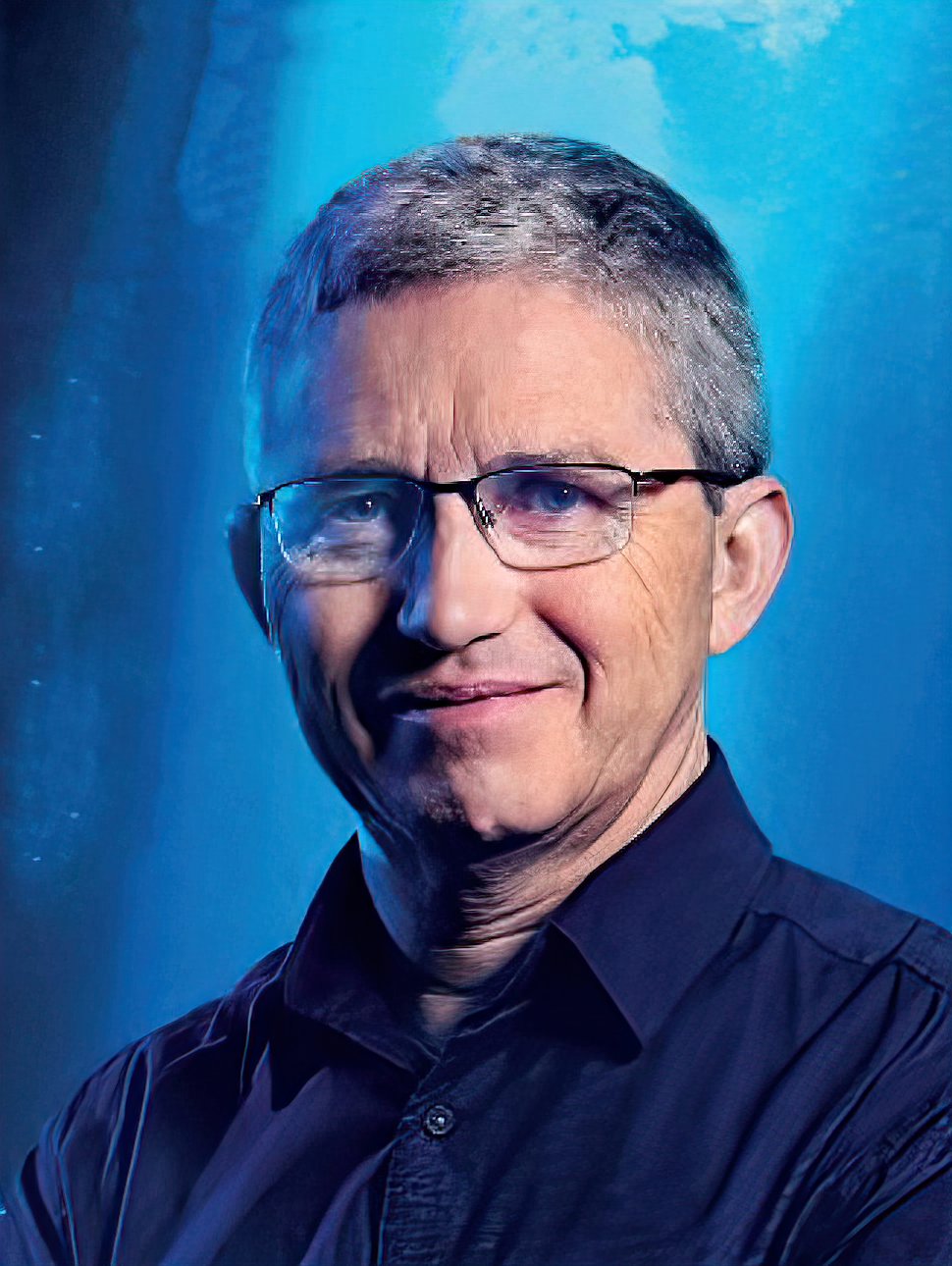 Person with short hair, glasses and navy blue collared business shirt smiles at the camera as a headshot