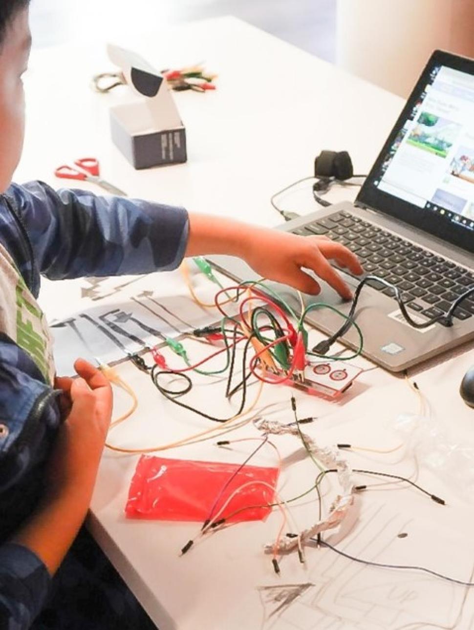 Image shows a young person using a laptop and coding kit to create a musical instrument