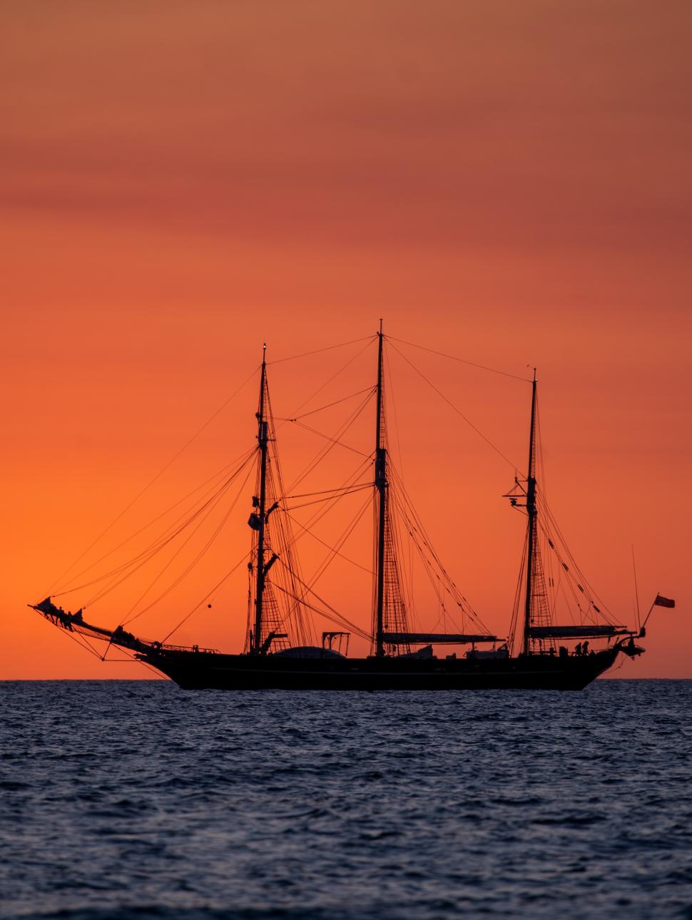 Image of an orange coloured sunset on the ocean with a yacht in silhouette