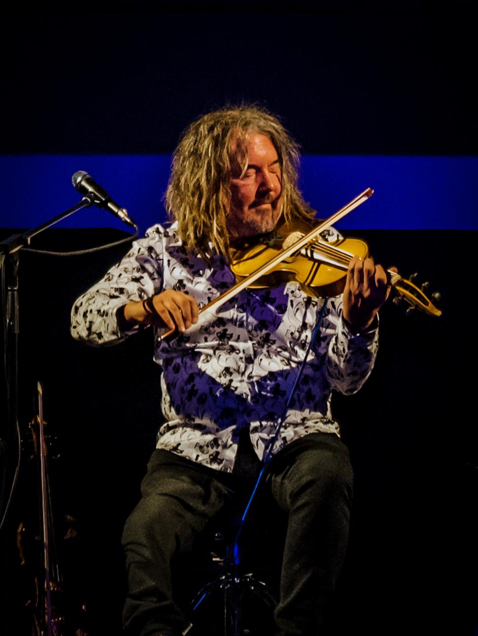 portrait shot of Rupert Guenther playing violin surrounded by stage lighting and microphone