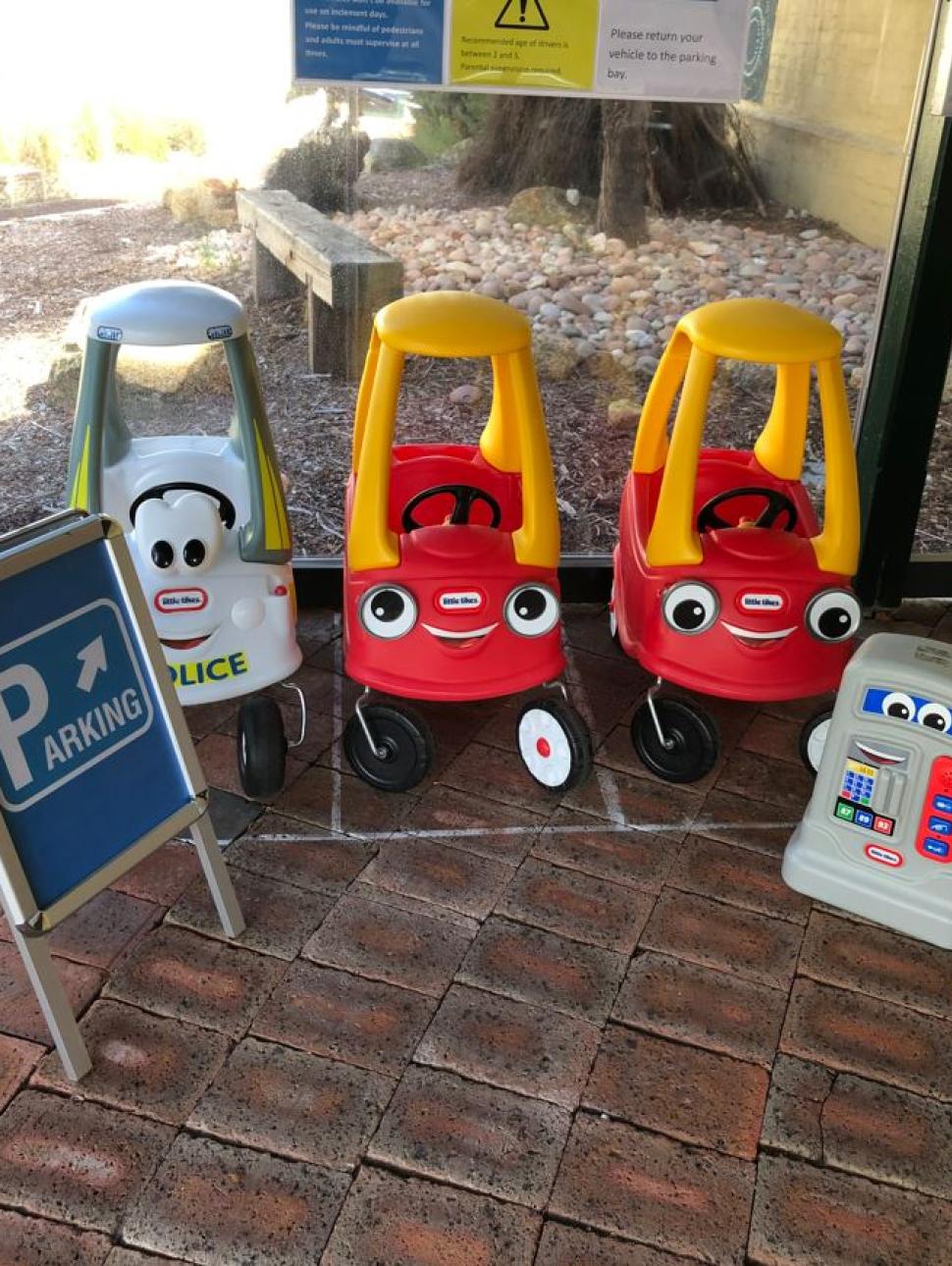 Three clasic kids cars parked alongside two traffic signs 