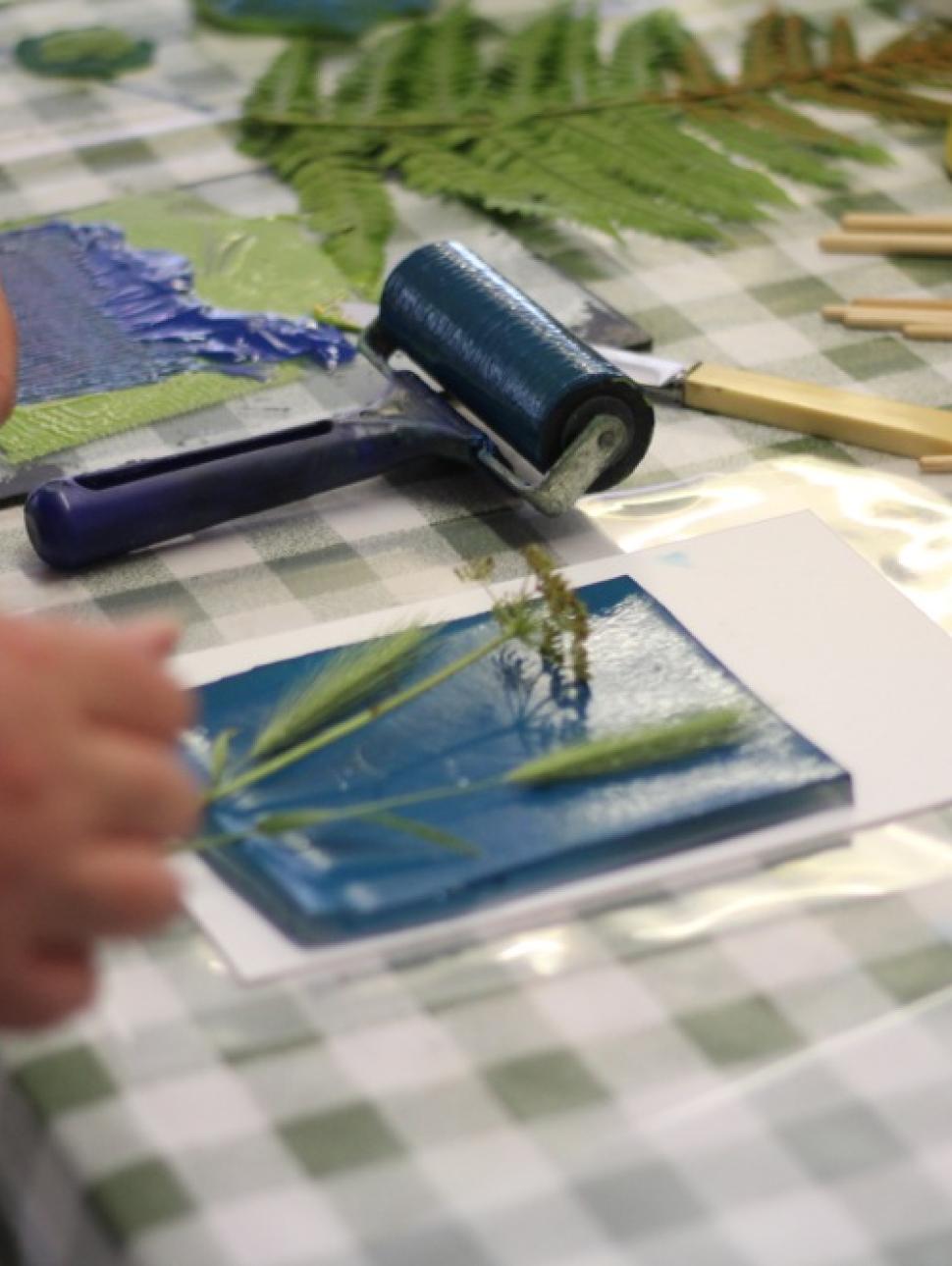Gell plate on white paper with leaves on stop and a paint roller on the left