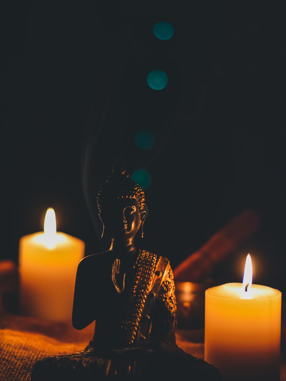 A Buddha statue in a darkened room, lit by two candles