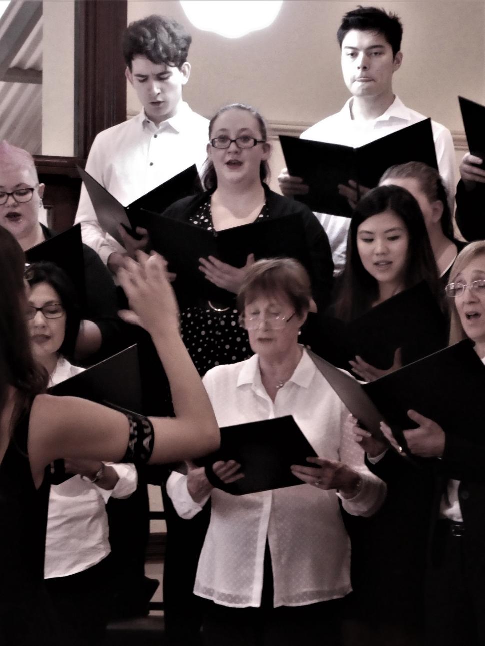 A diverse choir on risers sings to a conductor in the foreground