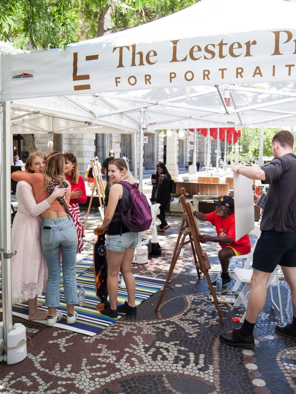 A public event marquee with participants chatting, hugging and painting