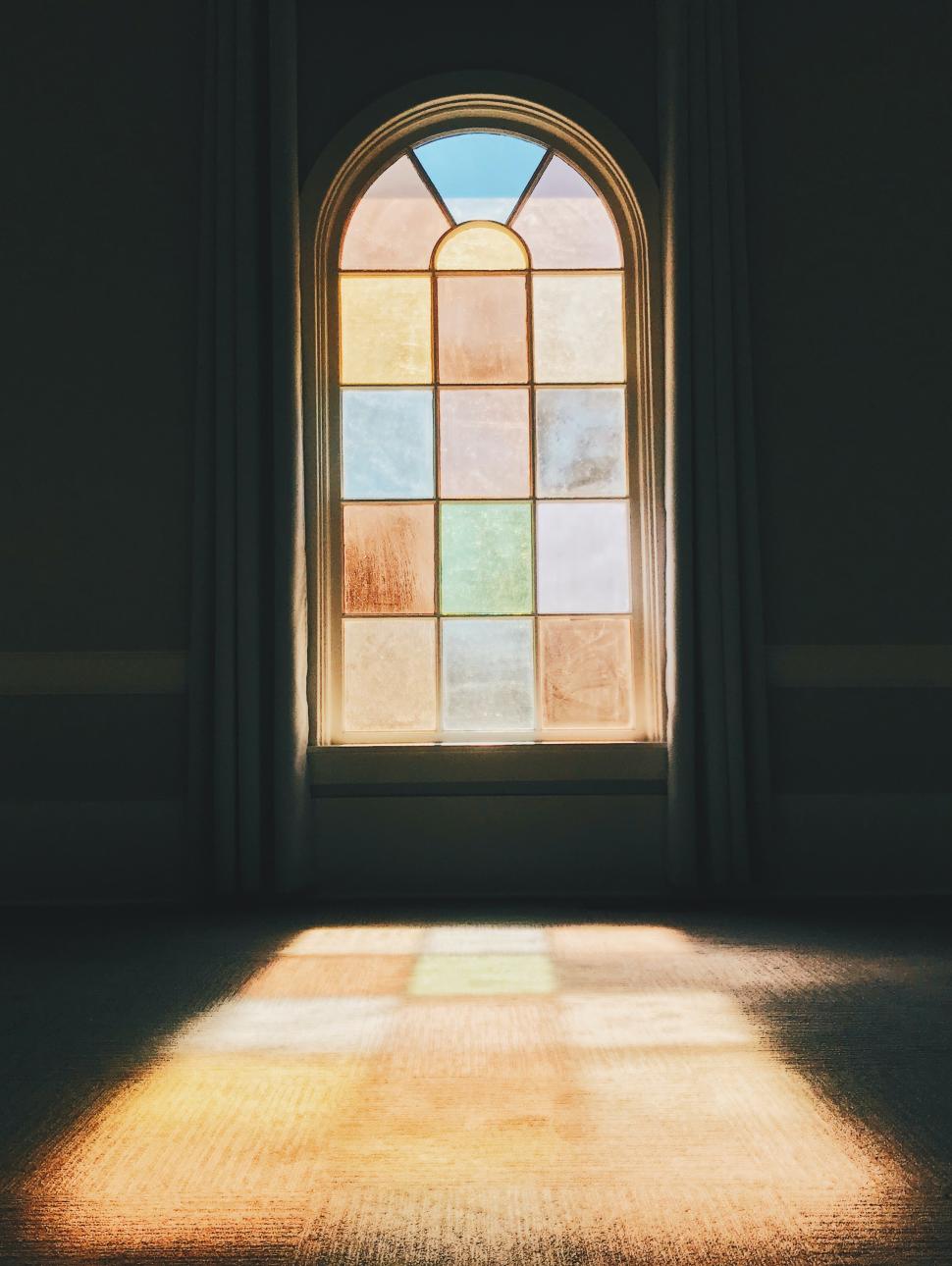 Stain glass window in dark room with light shining through coloured glass.