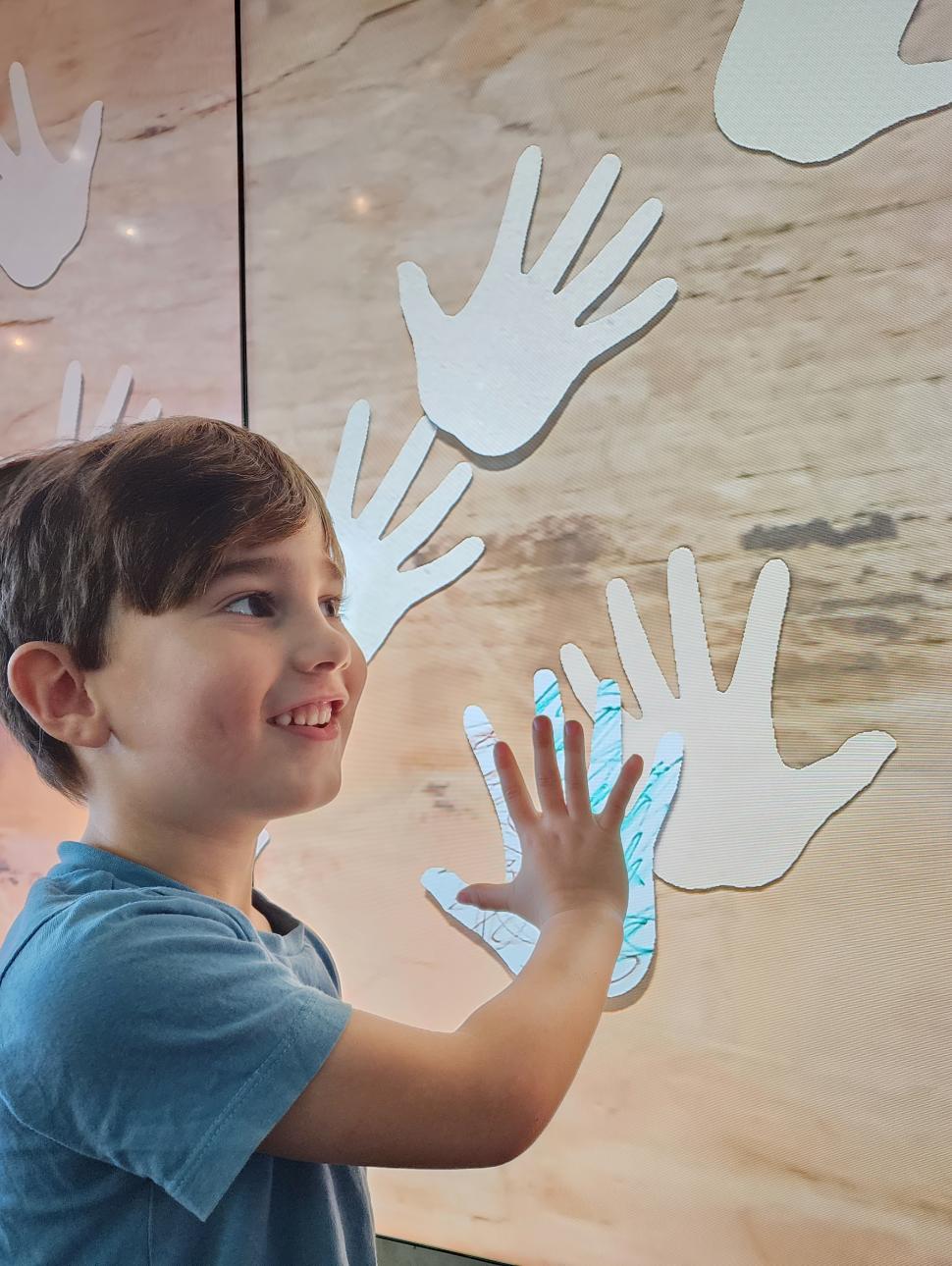 Young child puts hand up to a digital screen filled with hand prints