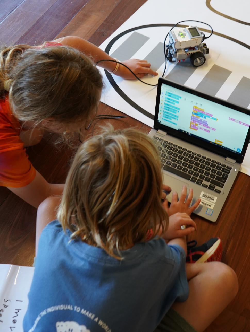 Image shows two children siting on the floor using a laptop computer to code a robotcoding 