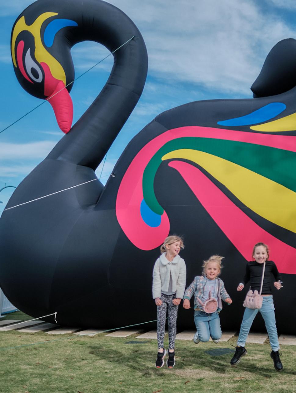 Large inflatable black swan picture with 4 children happily jumping in front of it