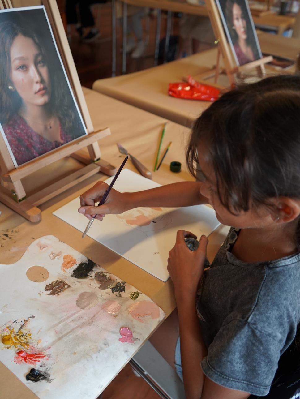 Image shows a young girl missing paint for a portrait she is painting