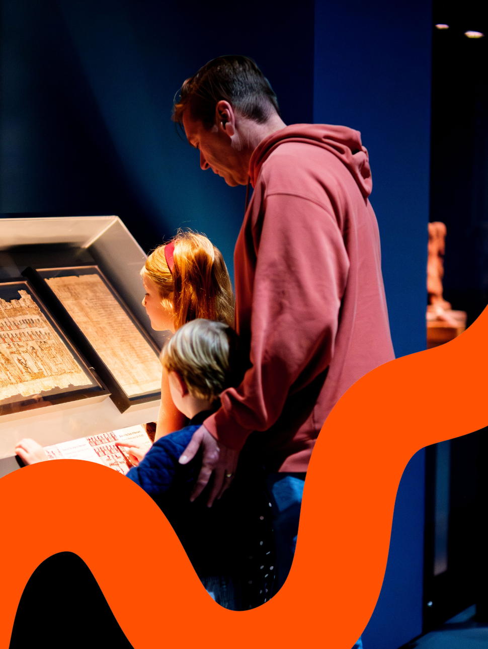 A family of three looking at pages from the Book of the Dead behind glass.