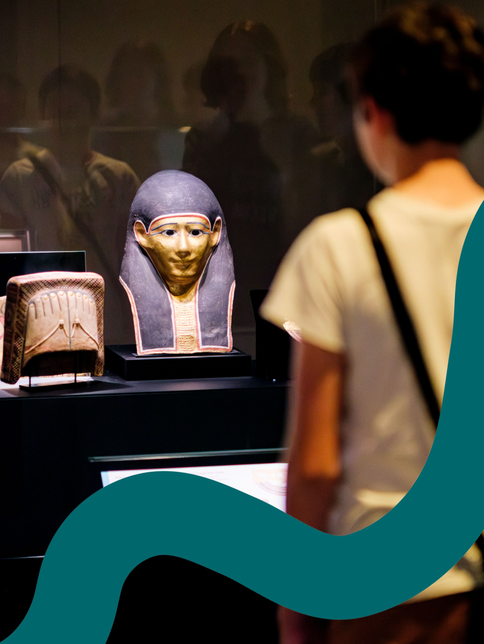 A young child standing in front of a display cabinet looking at a mask sculpture