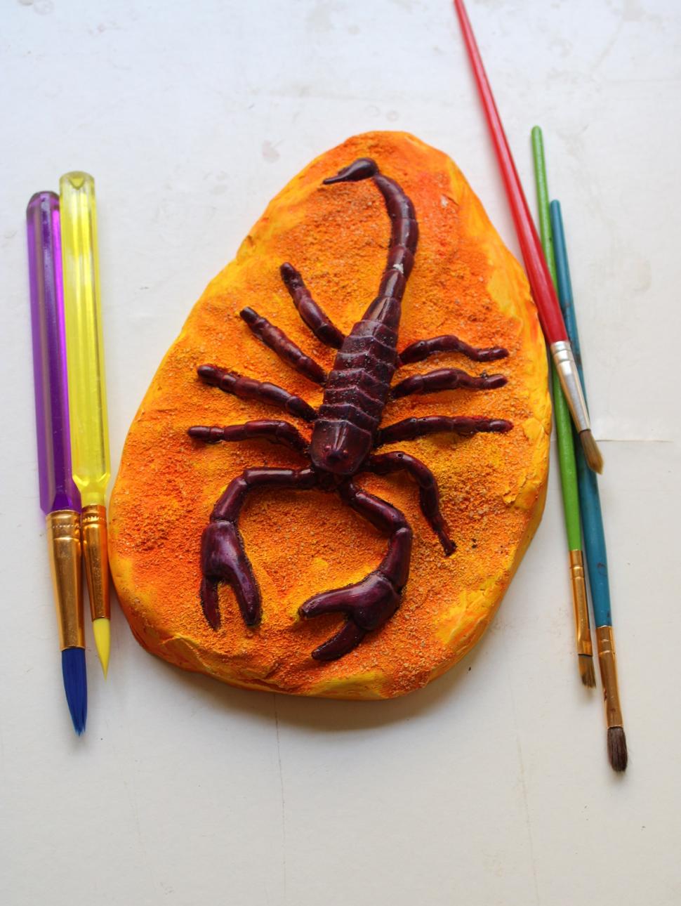 a scuplture of a scorpion painted orange with paint brushes on the sides