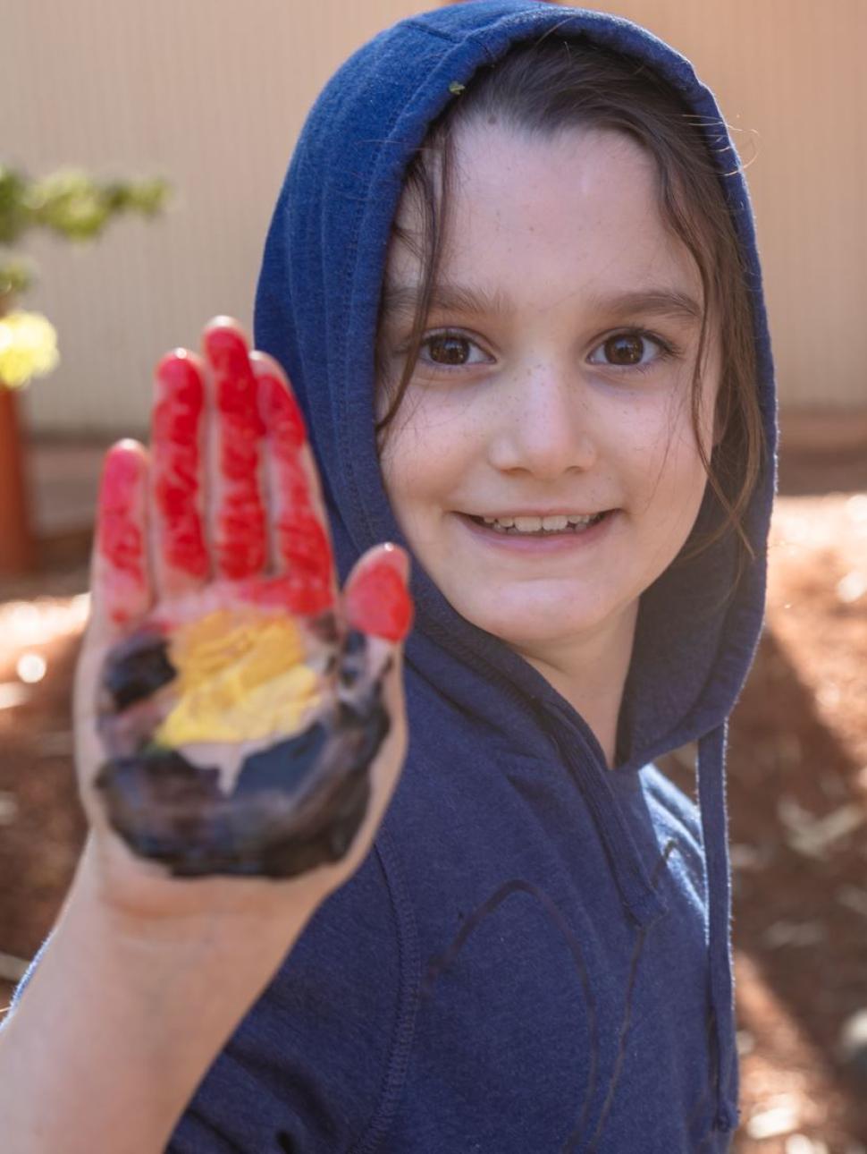 In the photo, a child's hand is held up with their palm facing outward, proudly displaying an Aboriginal flag painted within it. The colorful design symbolizes their connection to Indigenous culture and heritage.