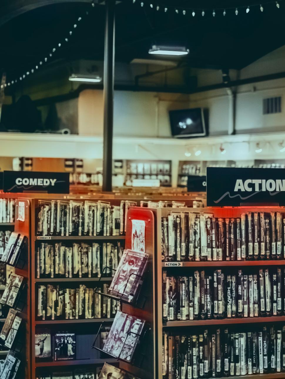 Image of VHS videos on a shelf display in a Blockbuster video store.