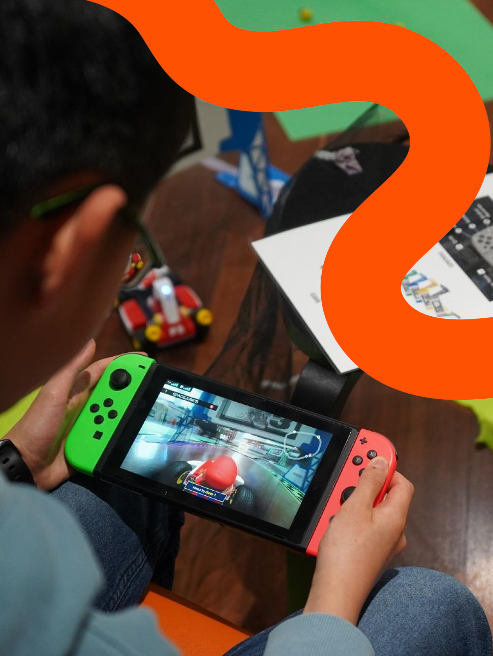 A child joyfully grips a game controller, immersed in a Mario Kart race, while an orange squiggle line adds a playful touch as a feature.