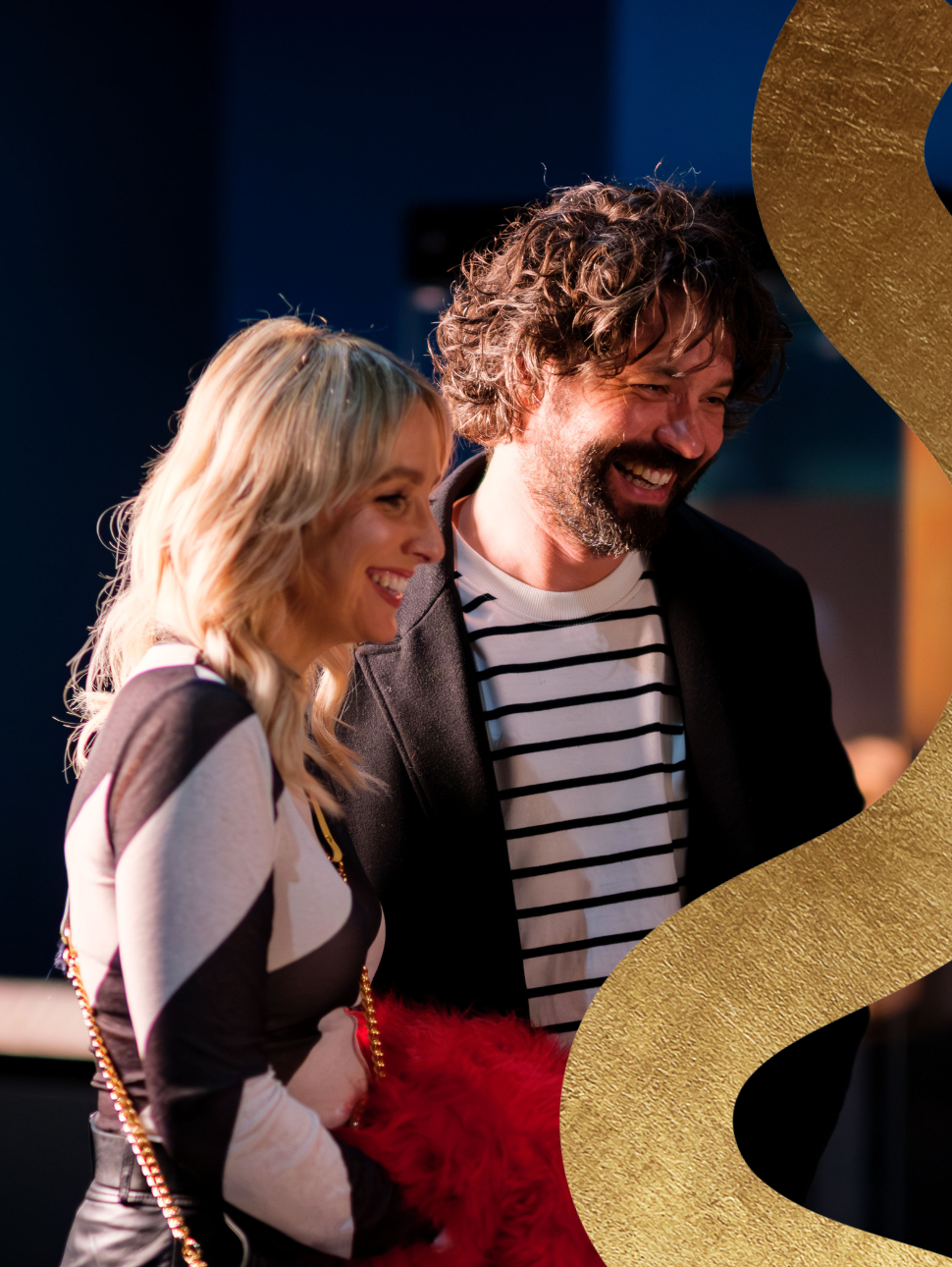 A happy couple shares smiles while admiring an exhibition, with a subtle golden squiggle feature in the corner.