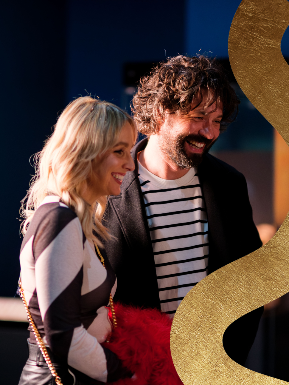  A happy couple shares smiles while admiring an exhibition, with a subtle golden squiggle feature in the corner.