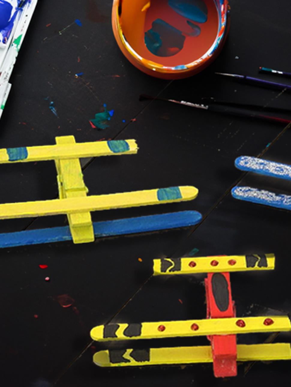 on a dark table there are three popsicle stick planes pained different colours