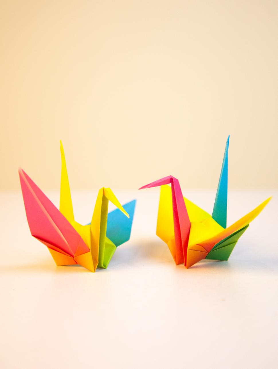 two multi coloured pieces of paper folded to look like a crane sit on a neutral coloured background