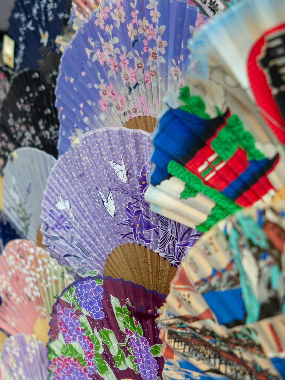 a large collection of coloured paper fans arranged on a wall next to eachother overlapping with different coloured designs