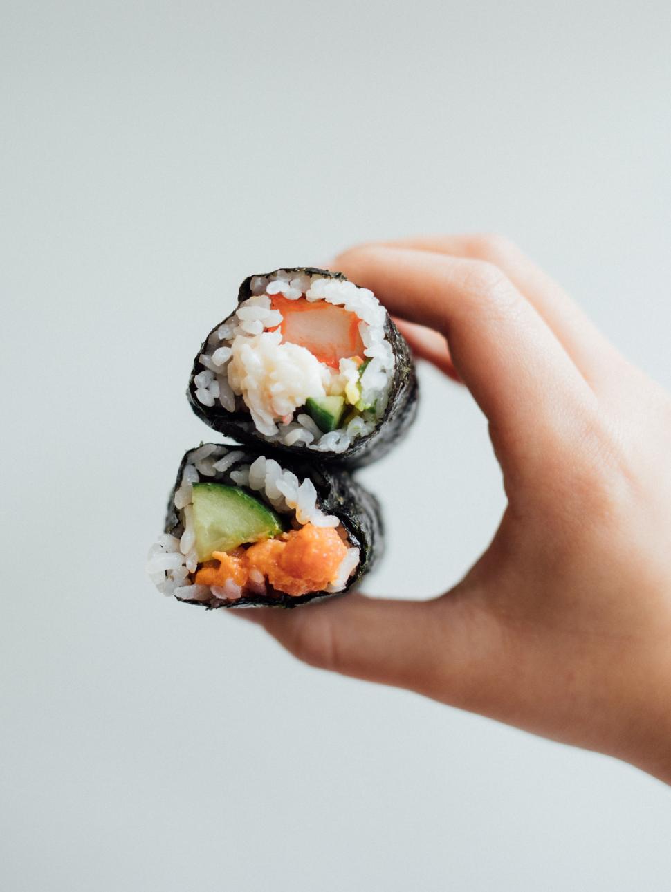 a child hand holds out two sushi rolls in one hand
