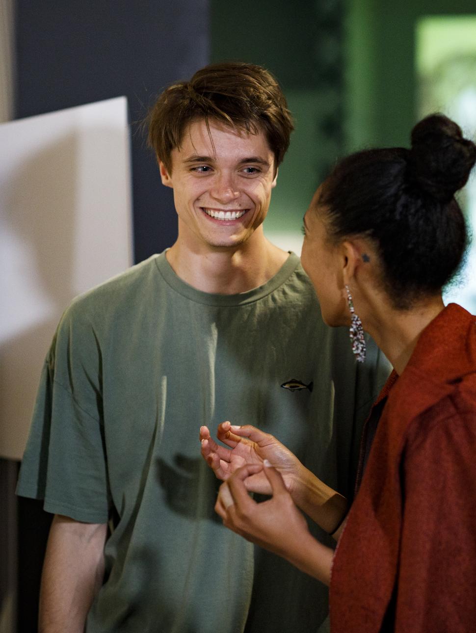 A young tall man in a green shirt speaks to a girl in red