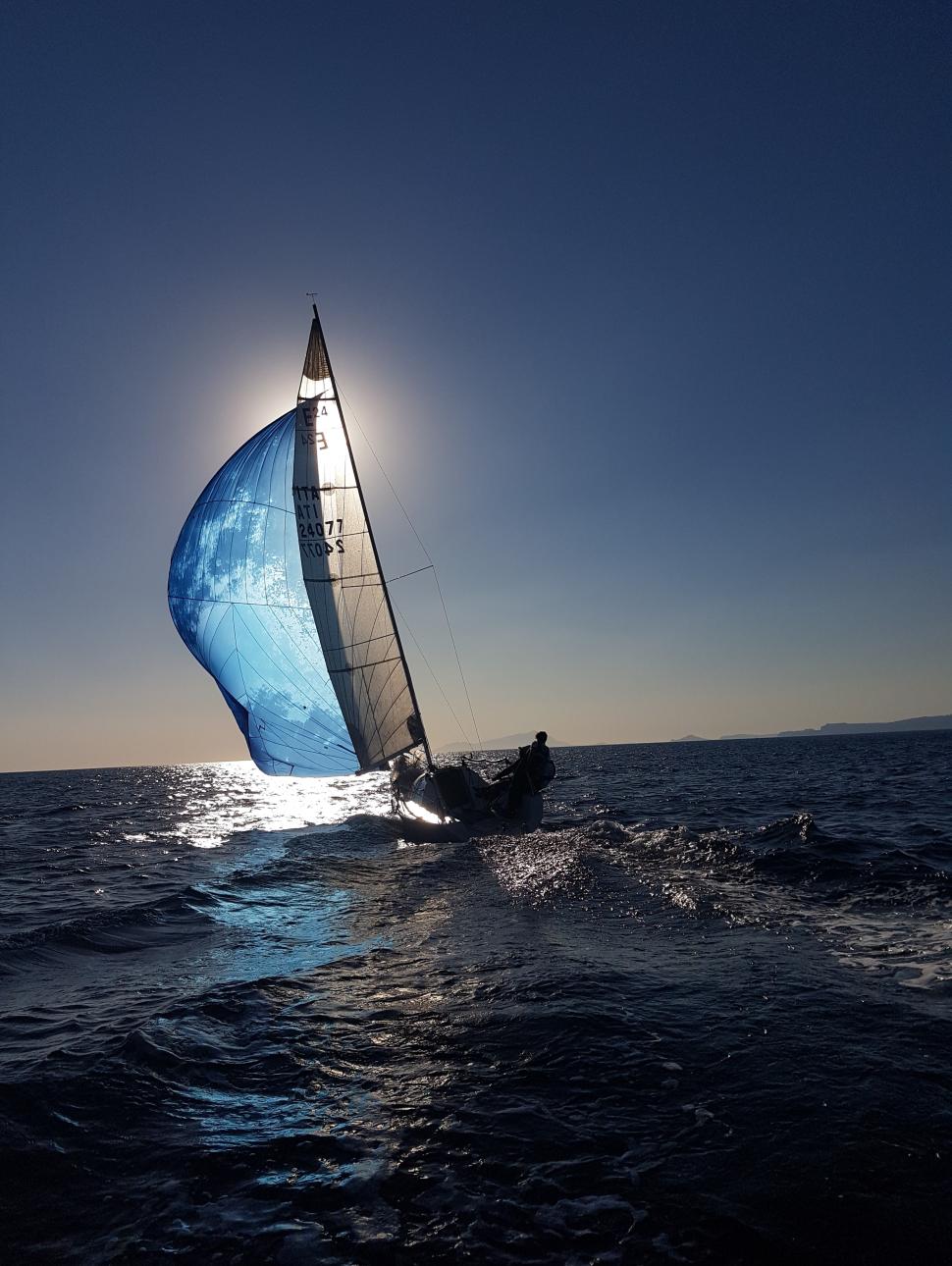 A person on a sailing boat with the sun setting behind the sail in front of themof
