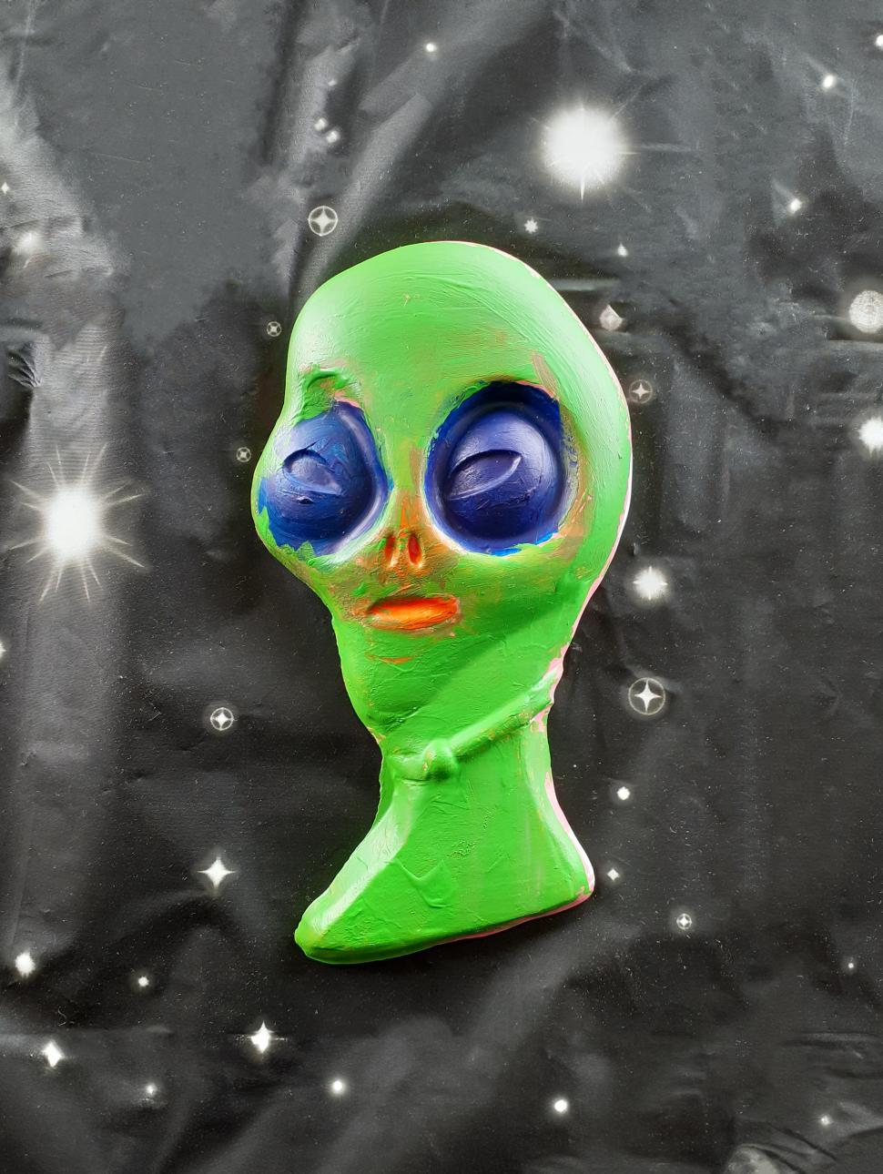 a green alien shaped head painted green on a dark space ackground