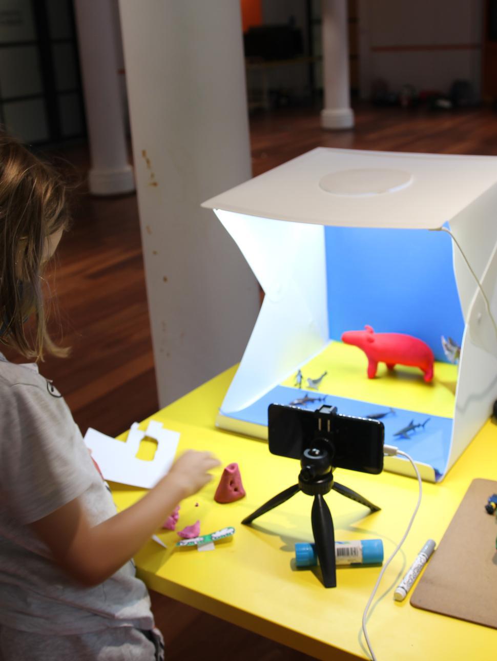a young child has set up a filming station on a table with lights, a mobile phone and small clay animals in a lightbox