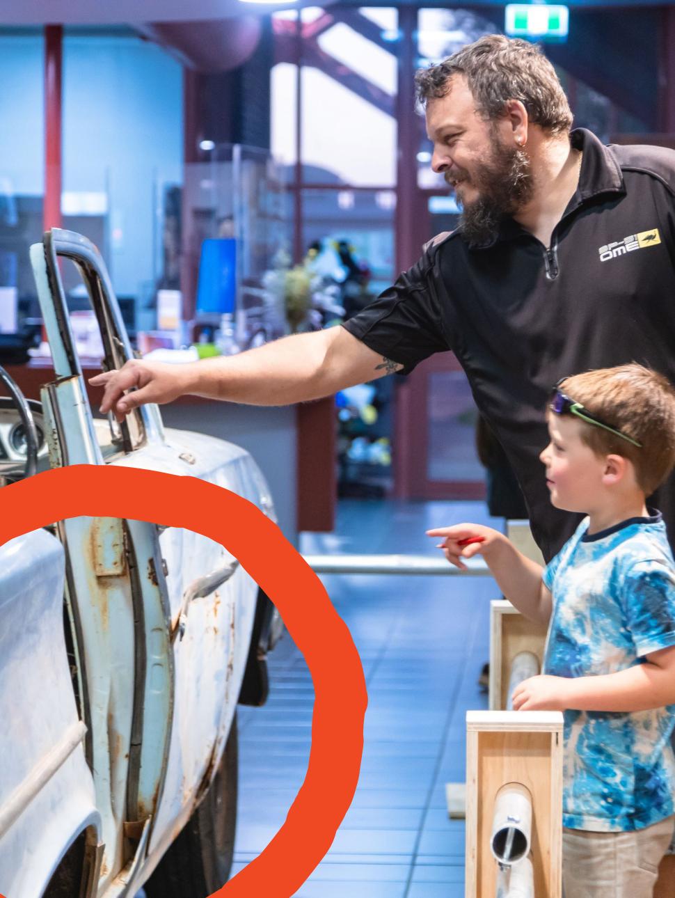 A father and his child look into a car on display, pointing and smiling