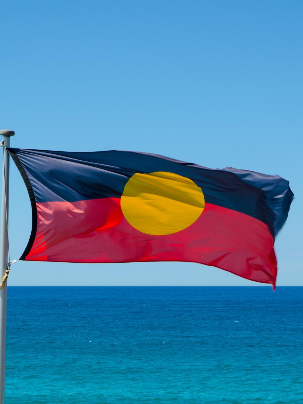 The Aboriginal and Torres Strait Islander flag flies against a bright blue sky
