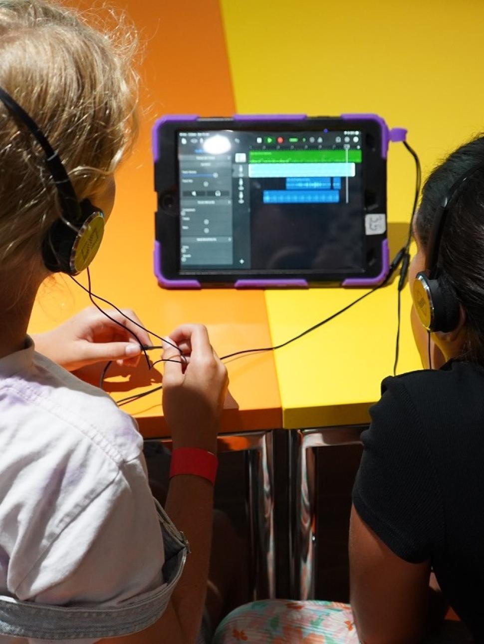 Image taken from behind two children who are looking at an iPad screen and using GaragBand to record sounds.