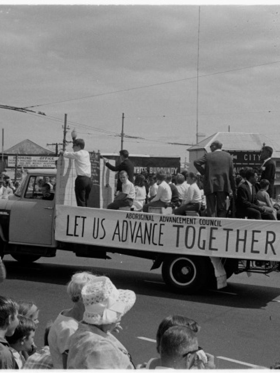 Archive photograph of crowds around a truck displaying sign 'Let us advance together'