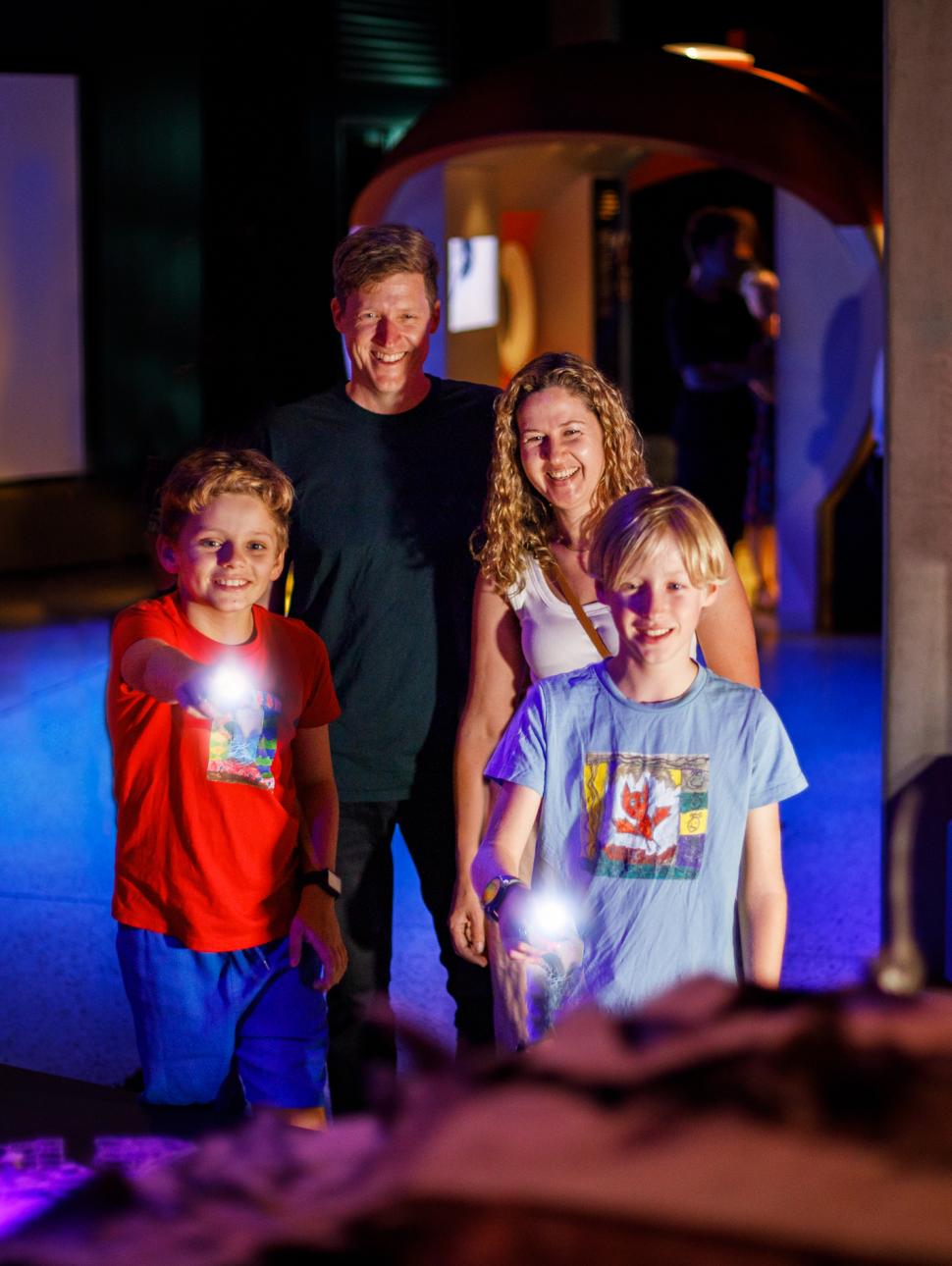 a family smiles and looks at a display in the exhibition while the younger children point with their small torches
