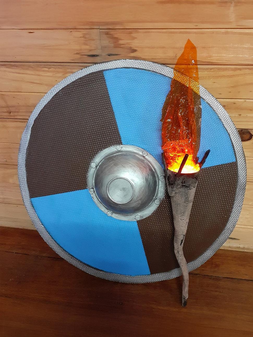 a made blue and dark grey shield resting against a wall along with a made viking torch with common objects