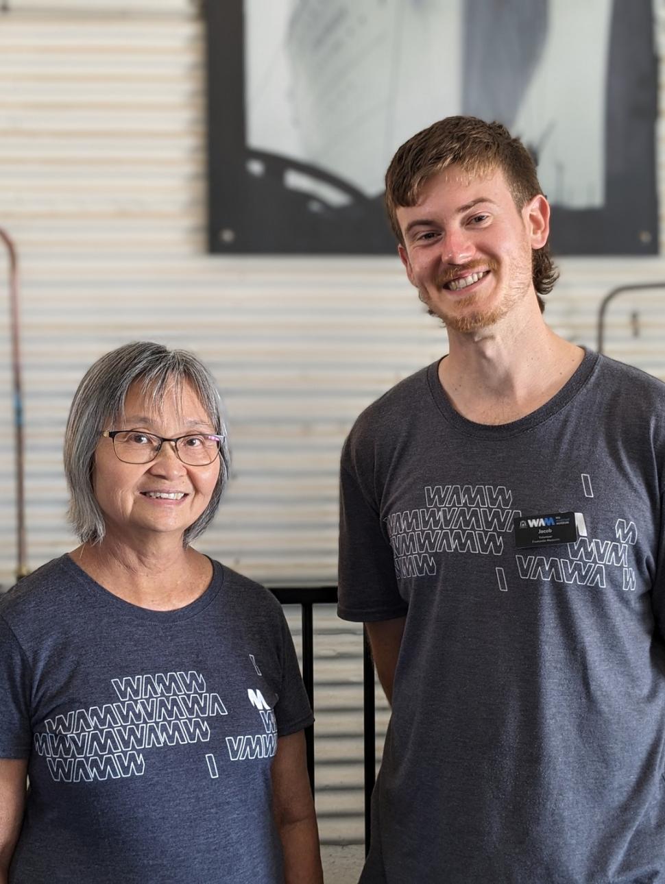 Two adult volunteers pictured in a workshop with a couple of steam engines partially displayed in the background. 