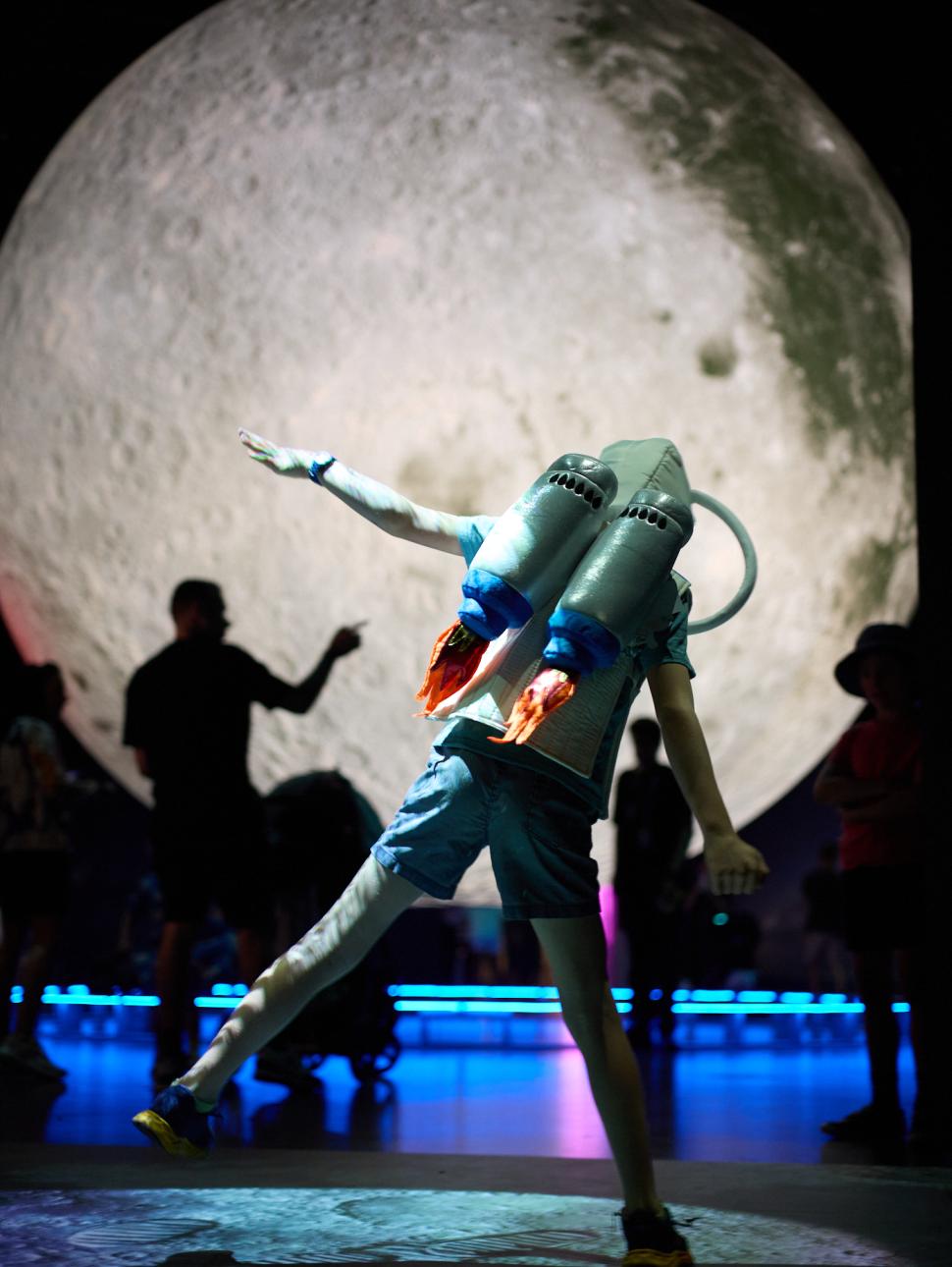 Child stepping to the right wearing a rocket bag with giant moon behind him