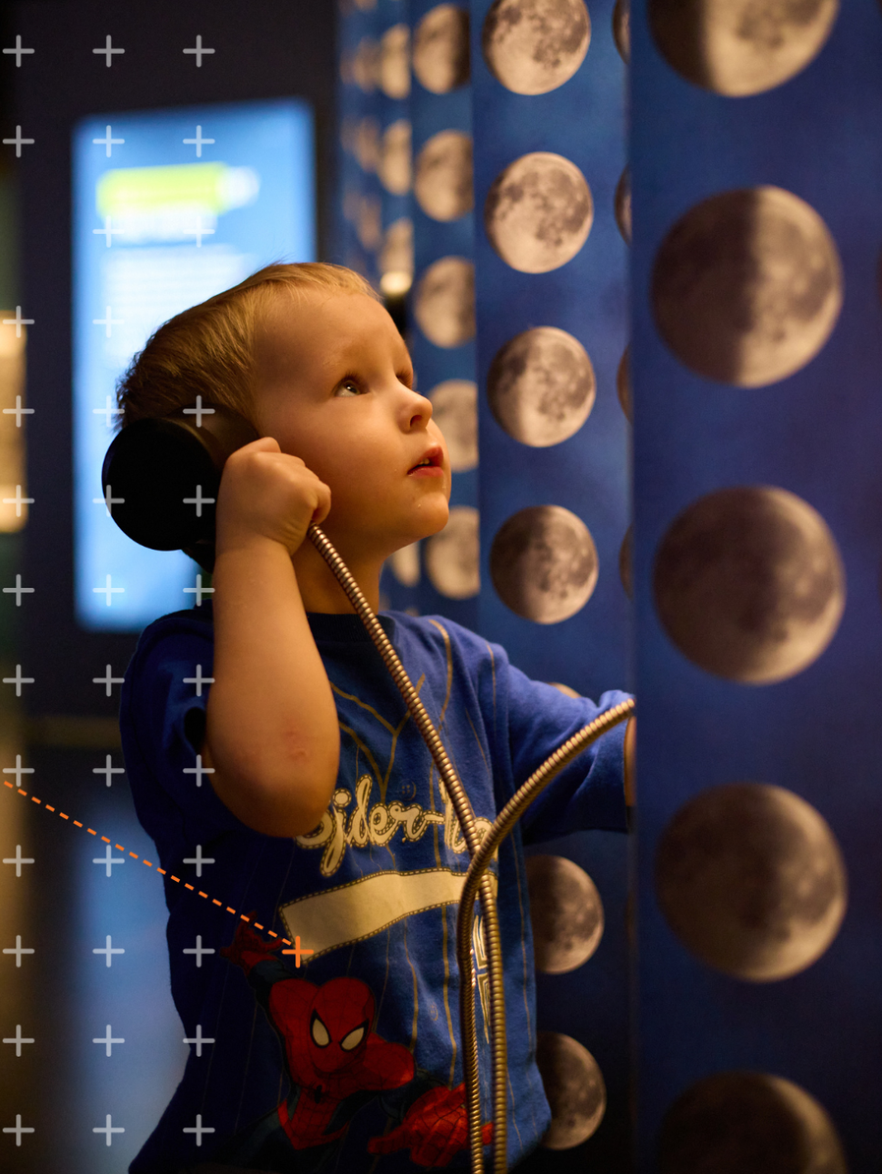  The image shows a young child holding a speaker to his ear with a moon pattern in the background.