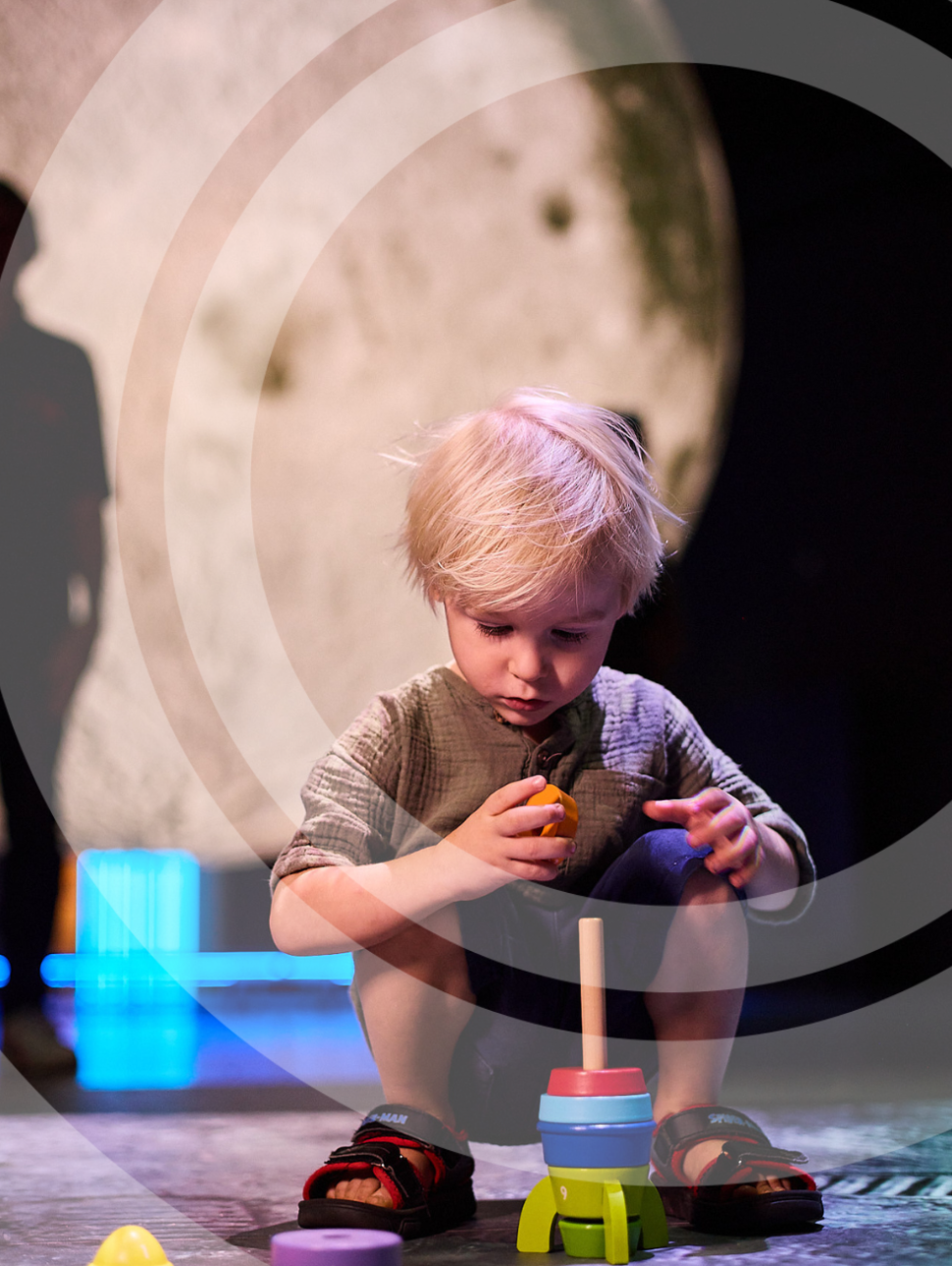  A young child playing with a vibrant rocket toy amidst a backdrop of a luminous, larger-than-life moon installation.
