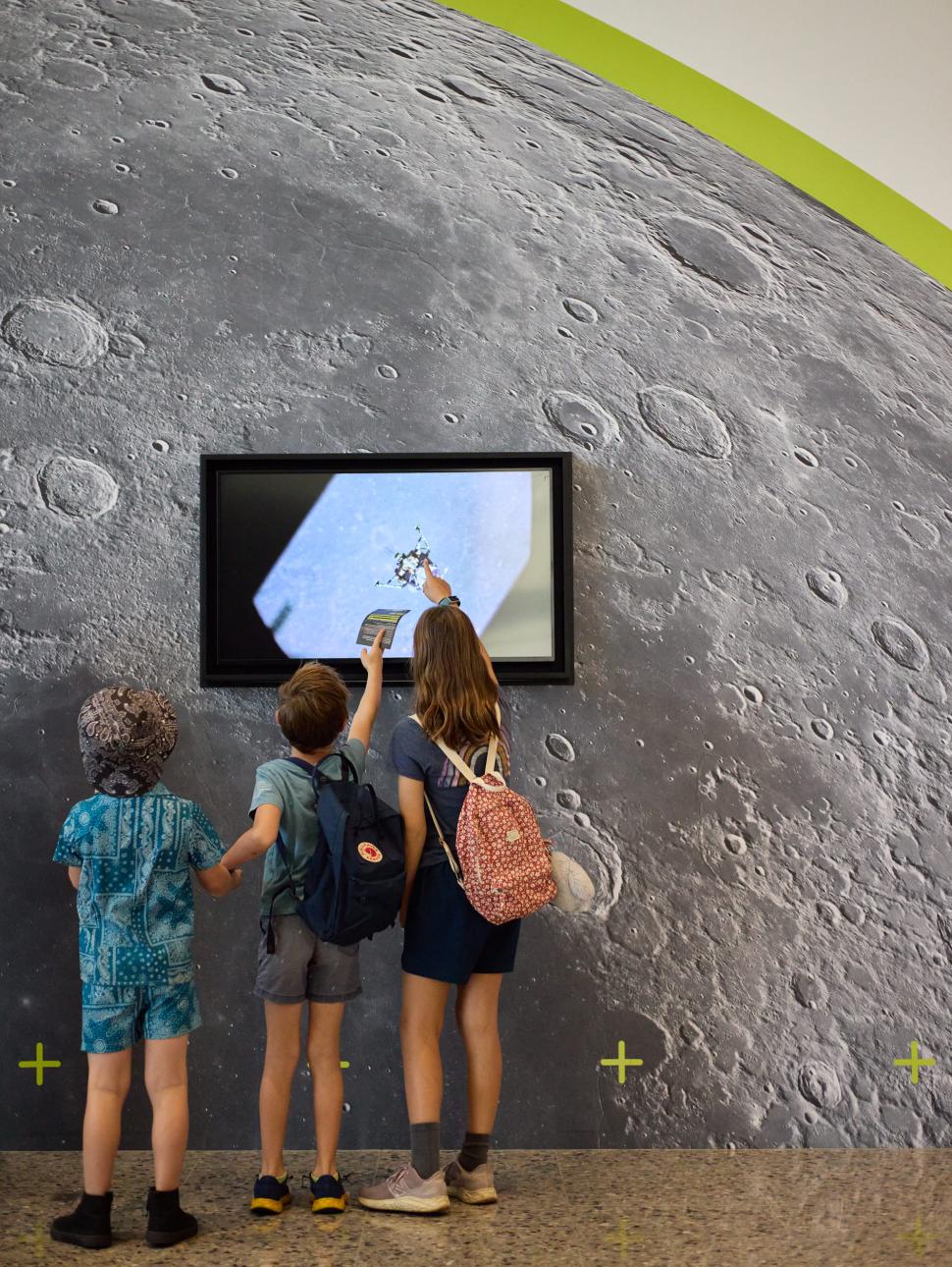 3 children stand in front a screen with moon images on it. 