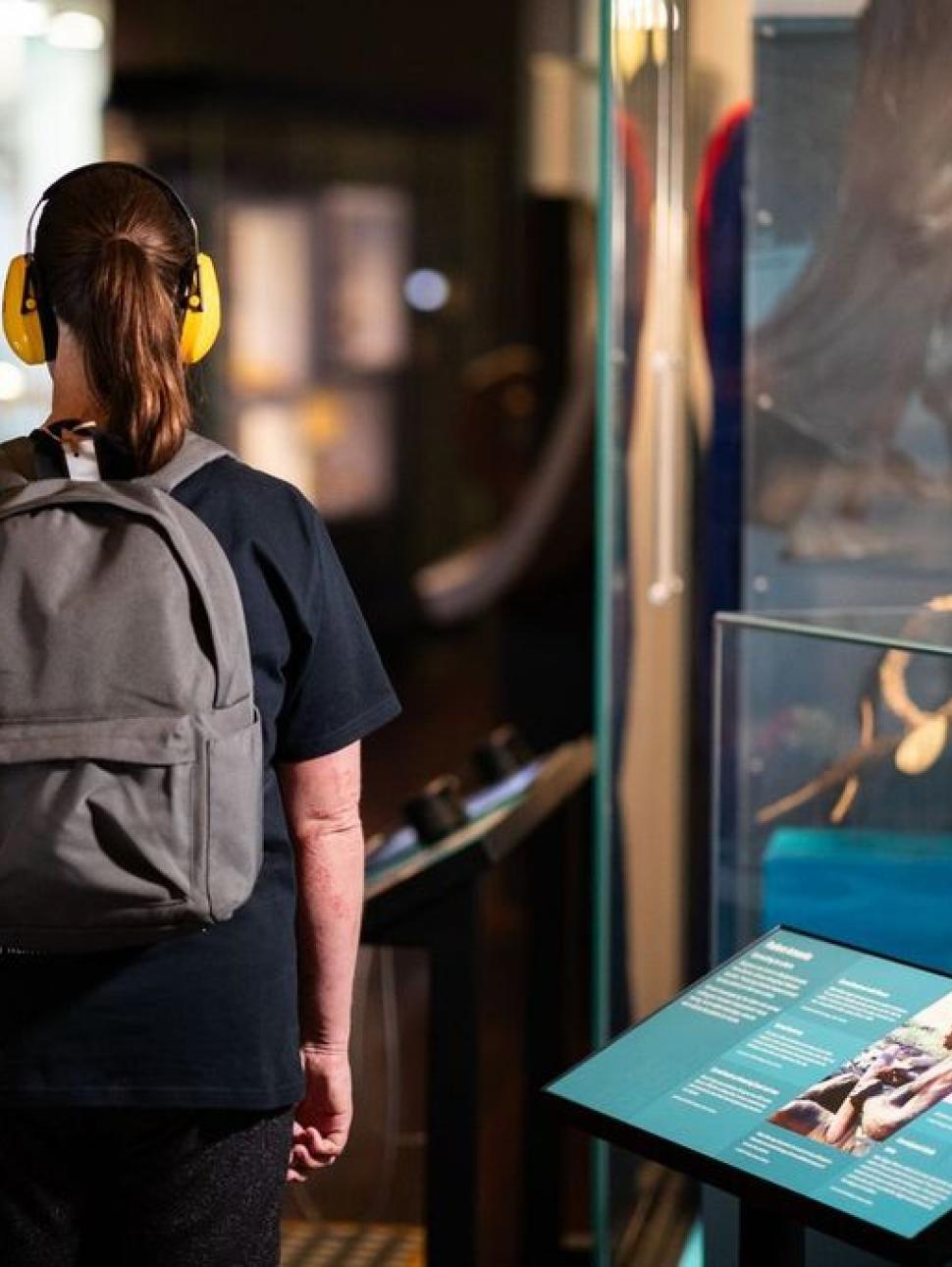 A woman wearing headphones examines a display of artifacts, immersing herself in the rich history they represent.