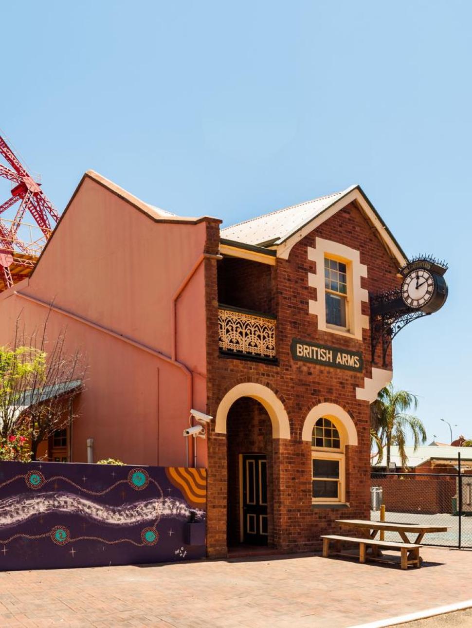 A tall brick heritage building with a clock and a metal frame in the background