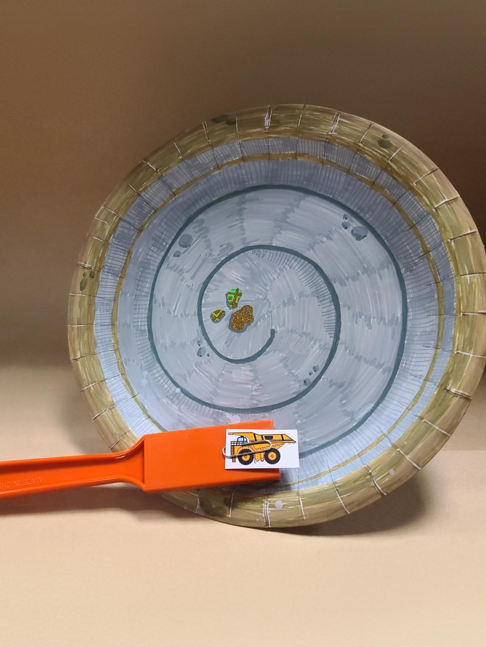 a decorated paper plate with a swirl pattern and an orange paddle sitting on the plate with a small picture of a mine truck clipped to the top of the paddle