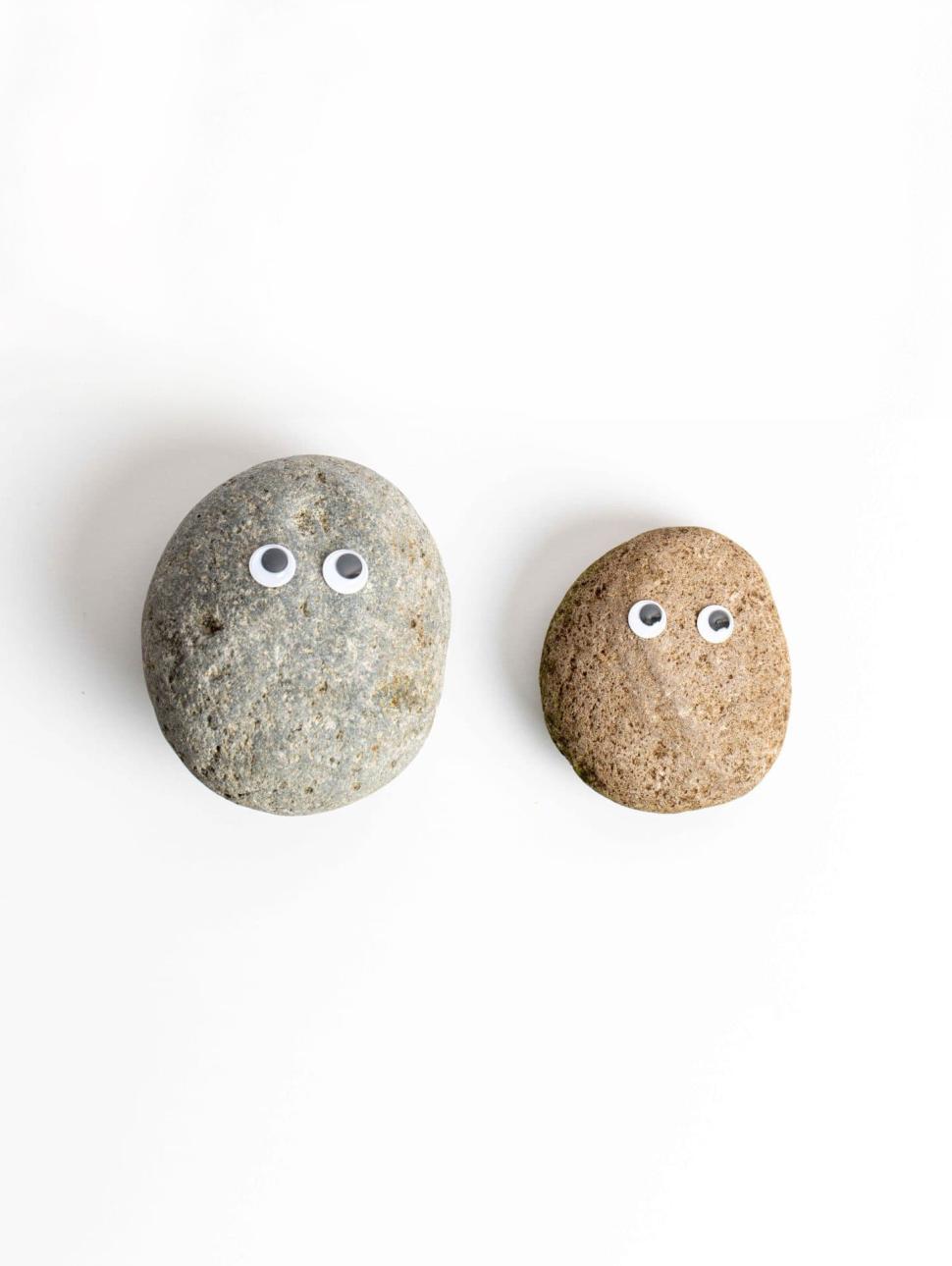 two smooth rocks have sets of eyes on them. they both sit on a white table 